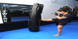Picture of a woman kicking a black heavy bag in the gym.