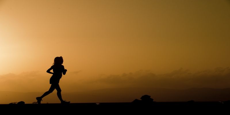 Image of a woman running with a yellowish background due to the sun setting.