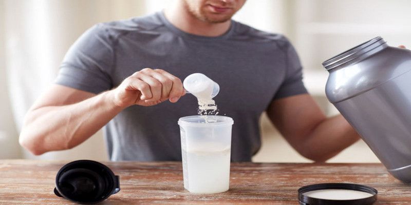 Picture of a man preparing a protein shake on a wooden table.