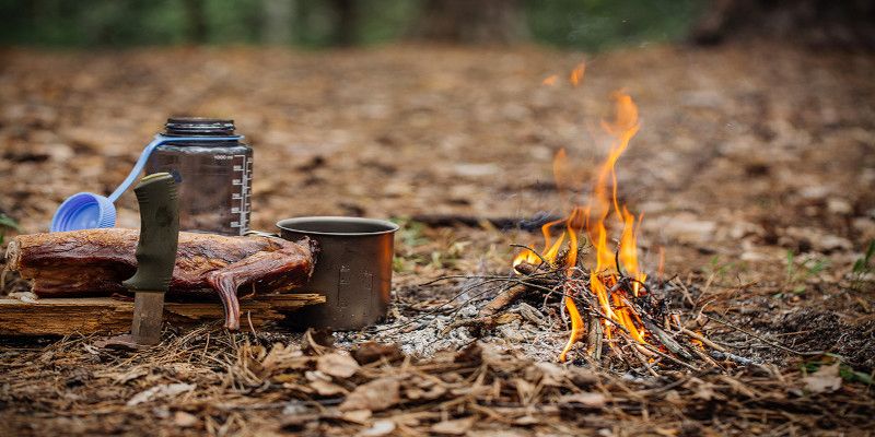 Image of survival gear and a fire outside in the woods.