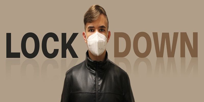 A man with a mask on with the word “lockdown” written behind him.