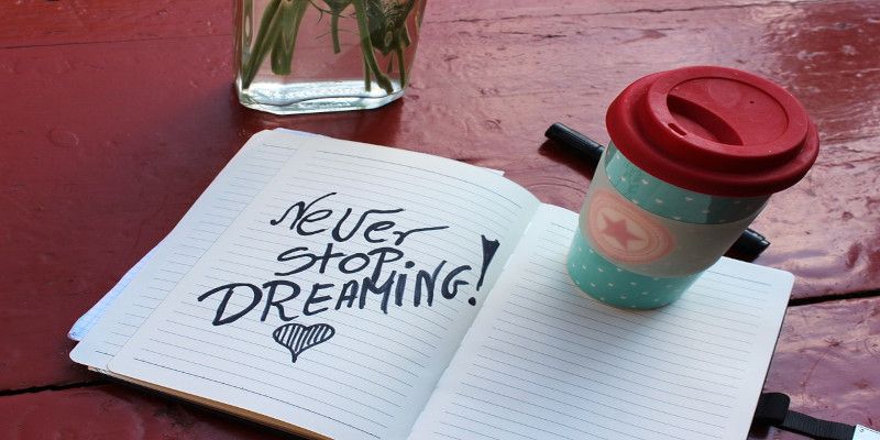 “Never stop dreaming” written in black letters in a notepad lying on a table with a coffee standing on top of it.