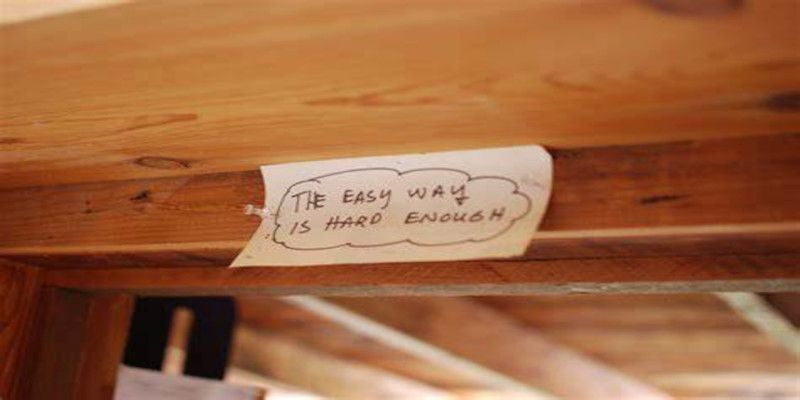 Image of a piece of paper reading, “the easy way is hard enough”, sticking against a hard piece of wood. 