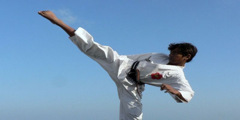 Picture of a man practicing martial arts outside. Performing a right high kick.