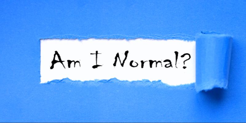 Image of the sentence, 'am I normal' written on a white piece of paper on a blue background.