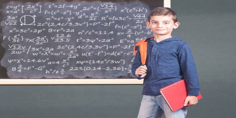 Image of a young child in school holding a book in front of a blackboard.