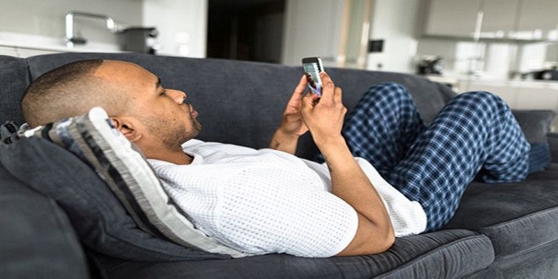 Image of a man looking at his cellphone while lying in the couch.