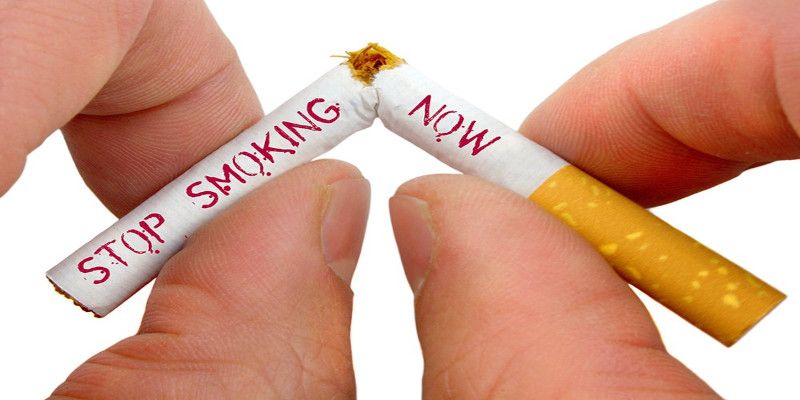Image of a person's hands breaking a cigarette in two with the words, “stop smoking now” written on the cigarette.