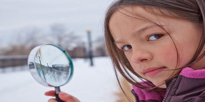 Image of a child observing her surroundings through a magnifying glass.