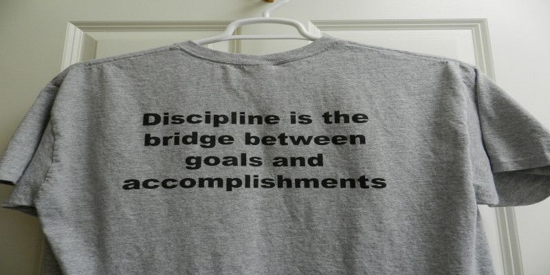 The quote, “discipline is the bridge between goals and accomplishments” written in black letters on a gray shirt.
