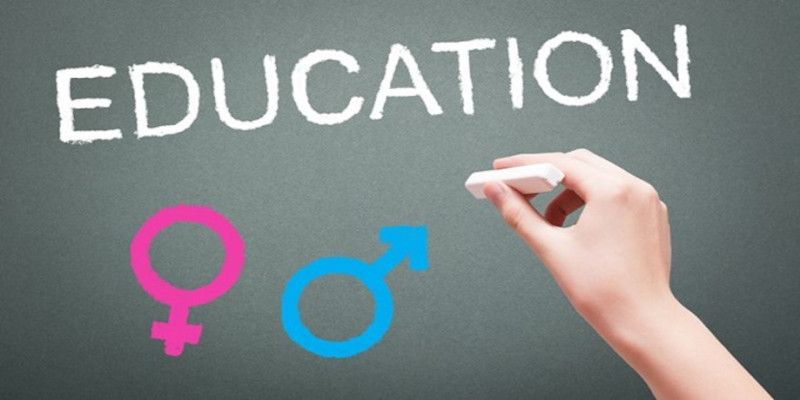 Image of a hand writing the word “education” on a board with chalk with a male and female sign underneath it.