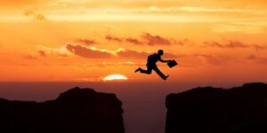 Image of a man jumping over a cliff while the sun is setting.