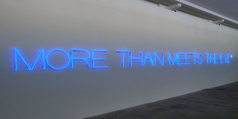 The quote, “more than meets the eye” hanging with blue letters against a white wall.