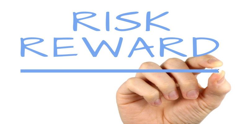 The words, “risk” and “reward” written by a blue marker by someone's hand on a white background.