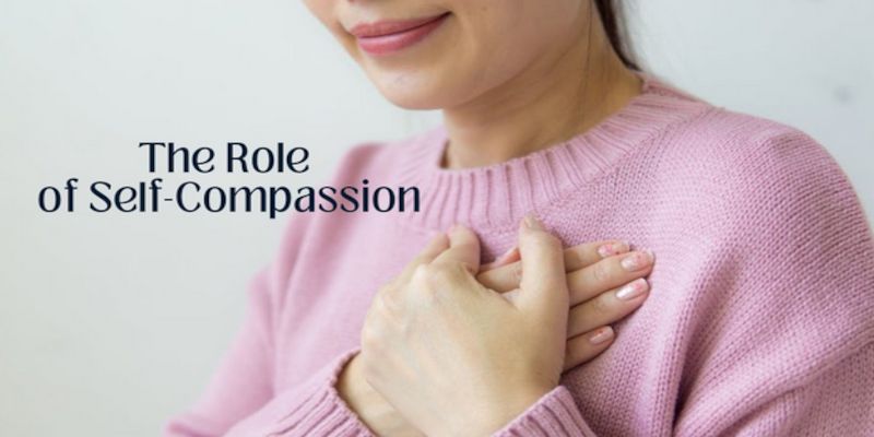 Image of a woman with a pink shirt crossing her hands in front of her chest with the words, “The role of self compassion” written in black letters in front of her.