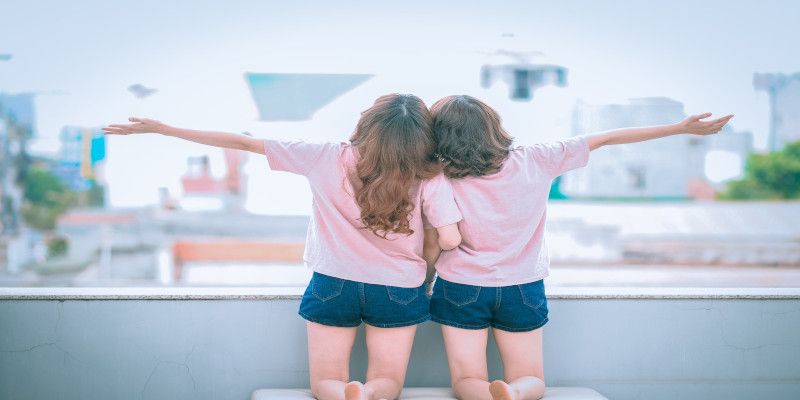 Image of two women wearing similar clothes hugging while extending their outer arm.