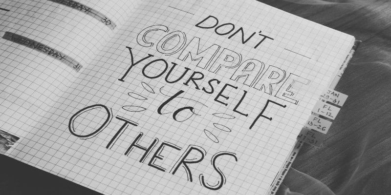 The quote, “don't compare yourself to others” written in black letters in a notebook.
