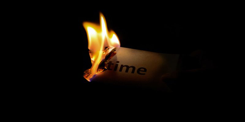 A piece of paper with the word “time” written on it being burned by fire.