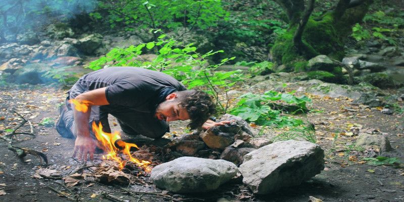Image of a man making a fire in the woods.