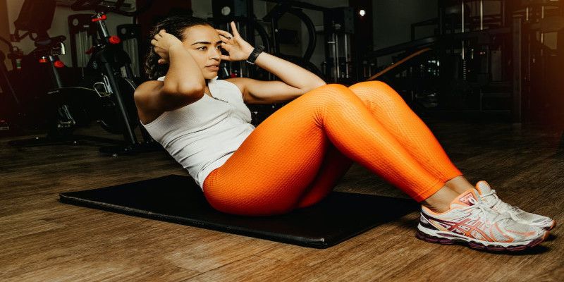 A woman with orange pants and a white shirt performing sit-ups.